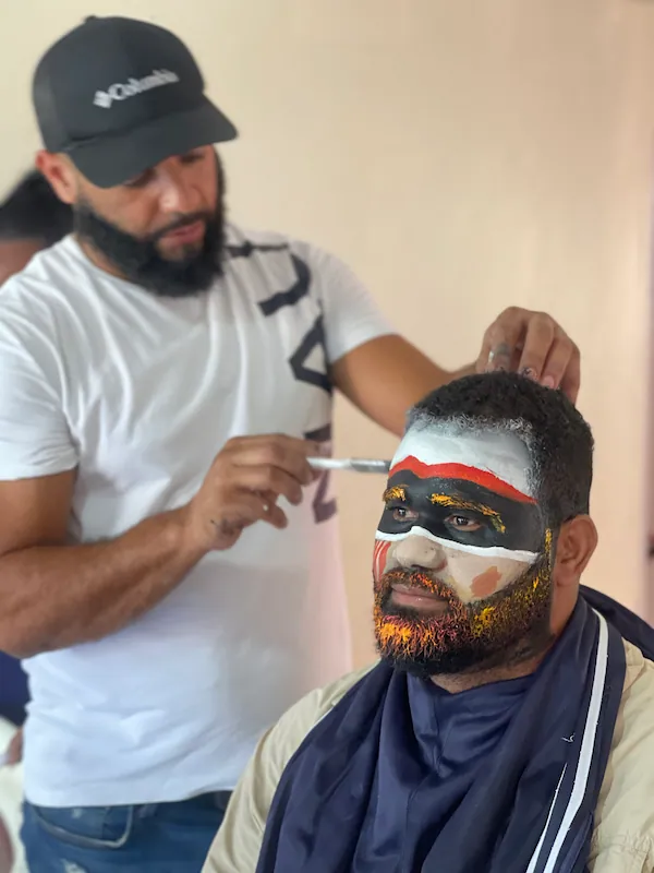 El artista Melvin Díaz pintando el rostro de Robinson Grullón para el personaje de Viajerito en el Carnaval Cotuisano.